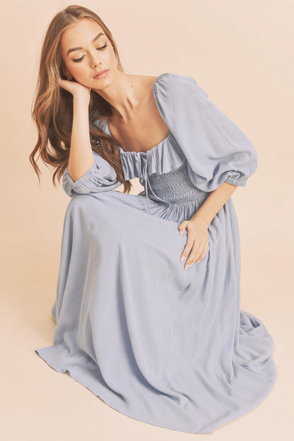 The Geri Dress boasts an eternally flattering shape, featuring a charmingly tied ruffled neckline, a smocked bodice, a lined skirt, and voluminous sleeves.