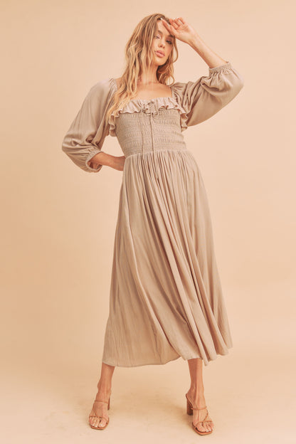 The Geri Dress boasts an eternally flattering shape, featuring a charmingly tied ruffled neckline, a smocked bodice, a lined skirt, and voluminous sleeves.