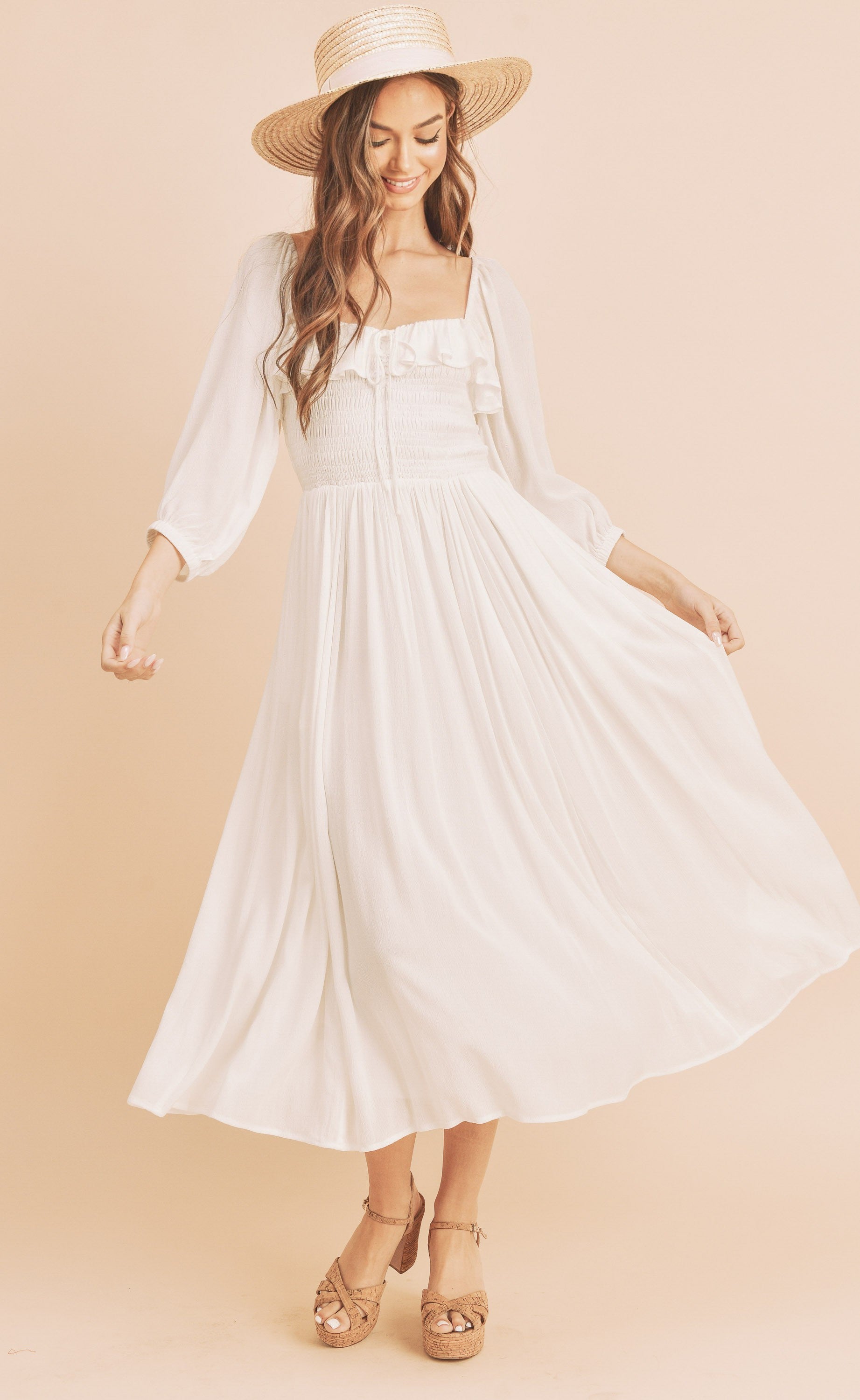 The Geri Dress boasts an eternally flattering shape, featuring a charmingly tied ruffled neckline, a smocked bodice, a lined skirt, and voluminous sleeves.
