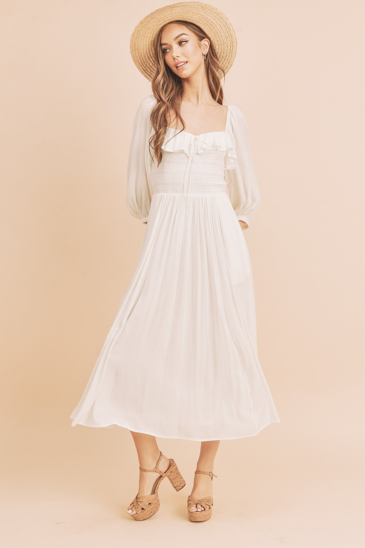 The Geri Dress boasts an eternally flattering shape, featuring a charmingly tied ruffled neckline, a smocked bodice, a lined skirt, and voluminous sleeves.