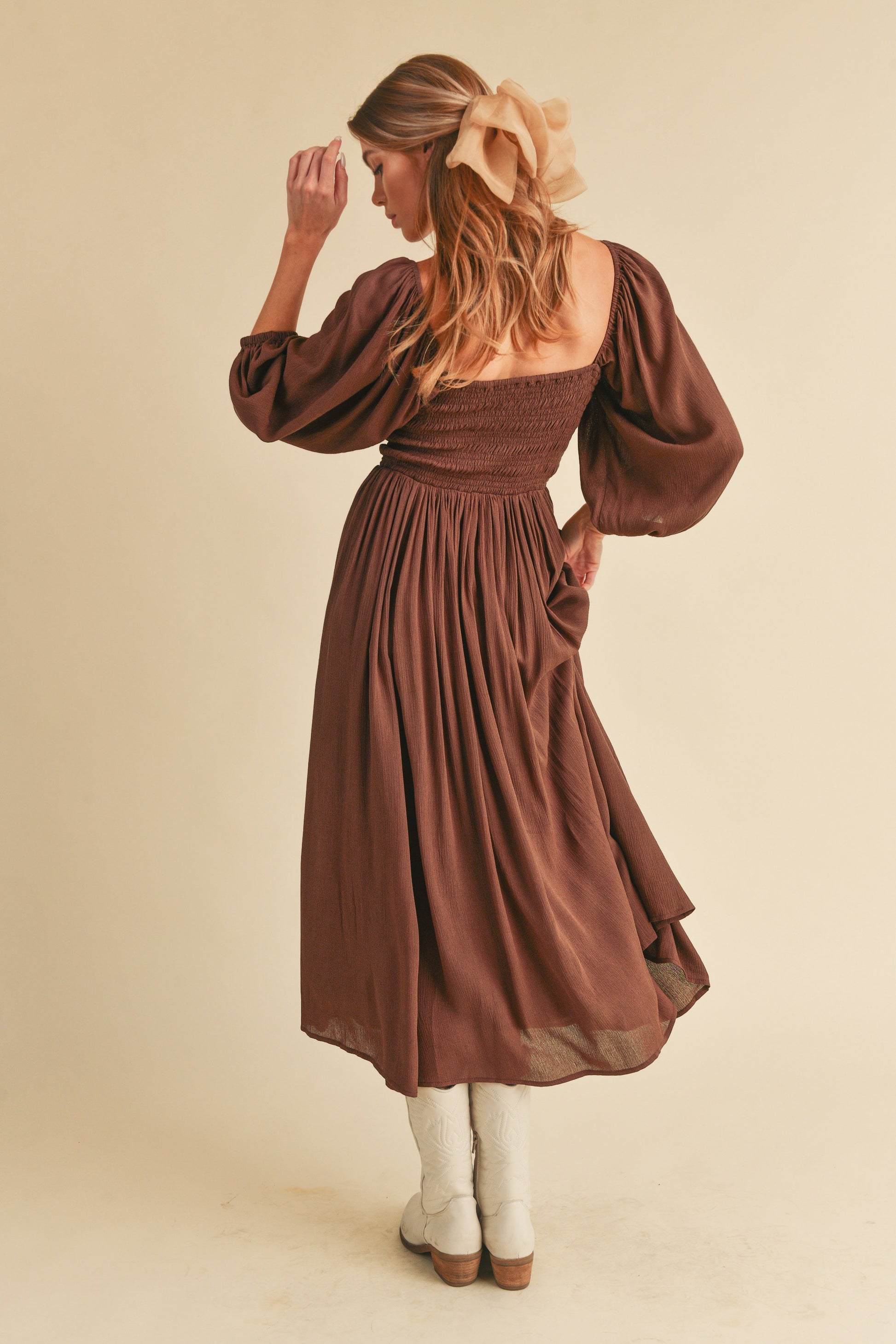 The Geri Dress boasts an eternally flattering shape, featuring a charmingly tied ruffled neckline, a smocked bodice, a lined skirt, and voluminous sleeves.