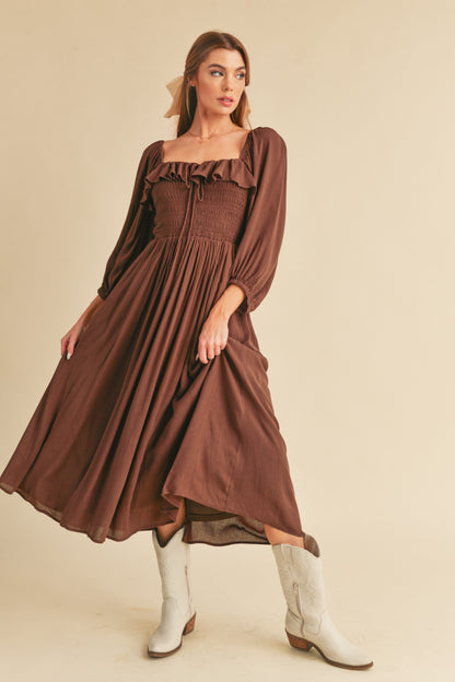 The Geri Dress boasts an eternally flattering shape, featuring a charmingly tied ruffled neckline, a smocked bodice, a lined skirt, and voluminous sleeves.