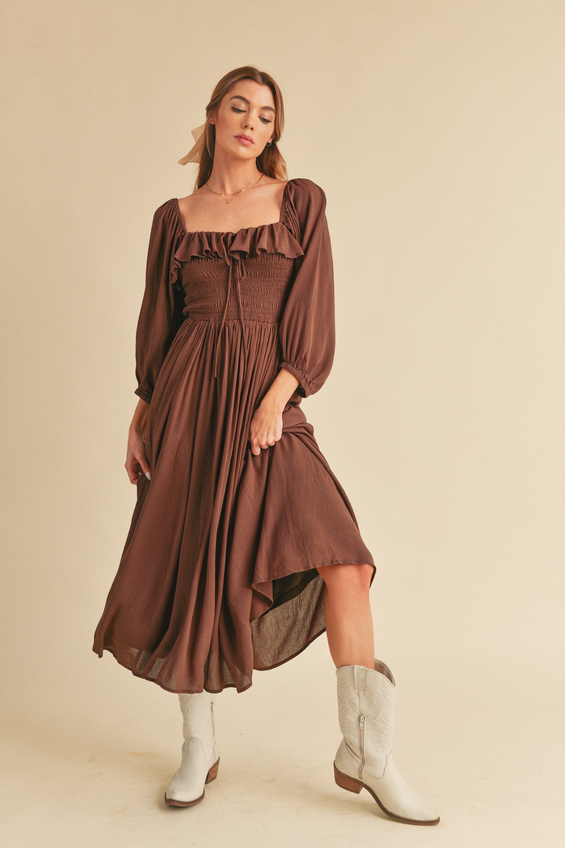 The Geri Dress boasts an eternally flattering shape, featuring a charmingly tied ruffled neckline, a smocked bodice, a lined skirt, and voluminous sleeves.