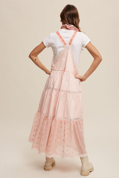 Step into summer romance with our Brooklynn Laced and Tiered Romantic Overall Maxi Dress. It features adjustable straps, a delicate kangaroo pocket, and embroidered crochet lace on the tiered skirt for a whimsical touch.