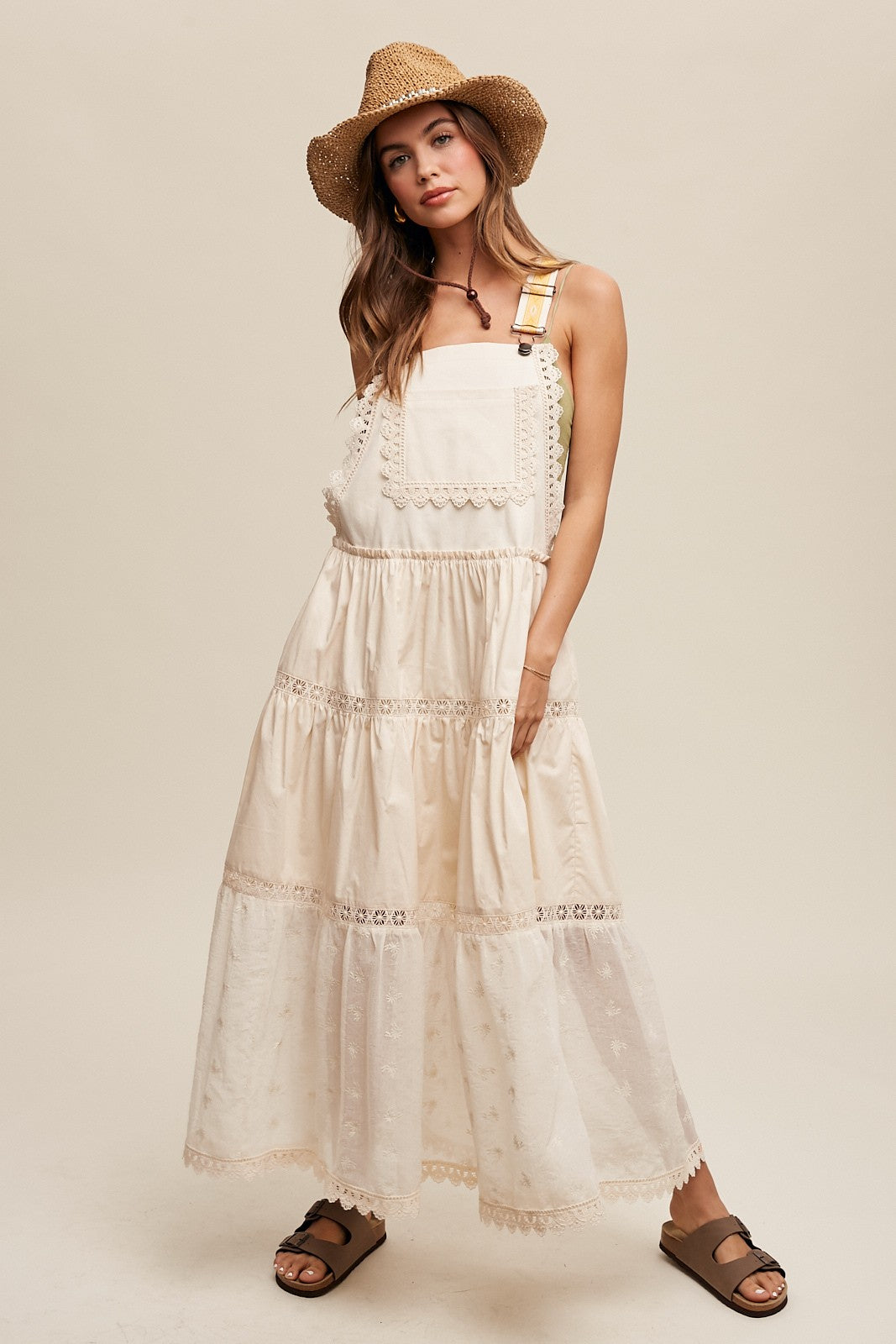 Step into summer romance with our Brooklynn Laced and Tiered Romantic Overall Maxi Dress. It features adjustable straps, a delicate kangaroo pocket, and embroidered crochet lace on the tiered skirt for a whimsical touch.