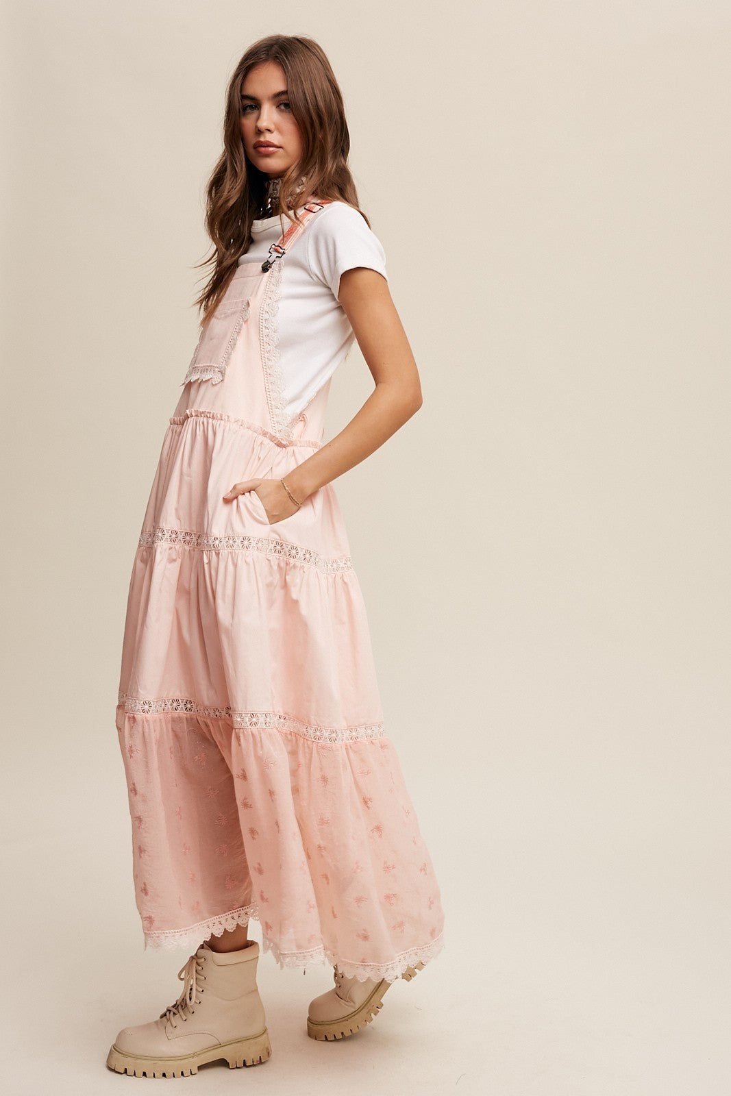 Step into summer romance with our Brooklynn Laced and Tiered Romantic Overall Maxi Dress. It features adjustable straps, a delicate kangaroo pocket, and embroidered crochet lace on the tiered skirt for a whimsical touch.