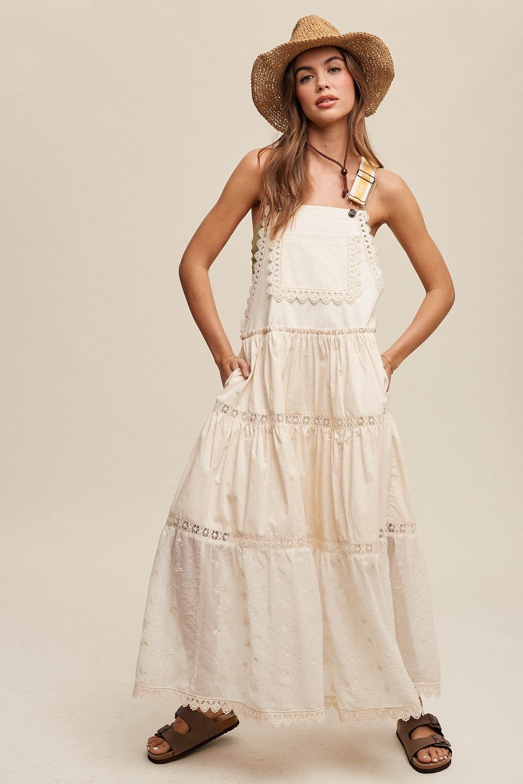 Step into summer romance with our Brooklynn Laced and Tiered Romantic Overall Maxi Dress. It features adjustable straps, a delicate kangaroo pocket, and embroidered crochet lace on the tiered skirt for a whimsical touch.