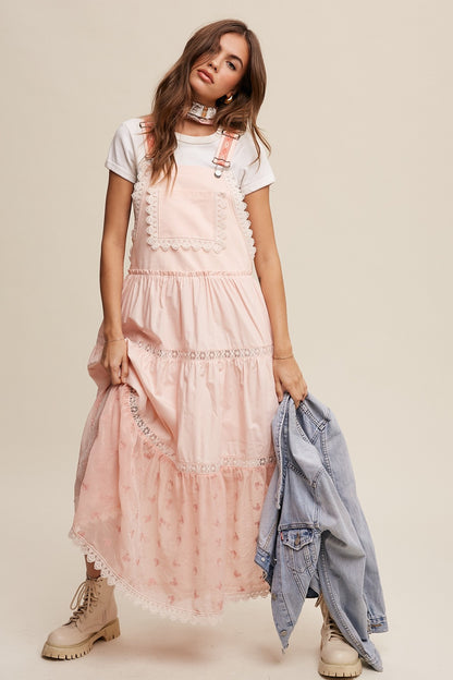 Step into summer romance with our Brooklynn Laced and Tiered Romantic Overall Maxi Dress. It features adjustable straps, a delicate kangaroo pocket, and embroidered crochet lace on the tiered skirt for a whimsical touch.